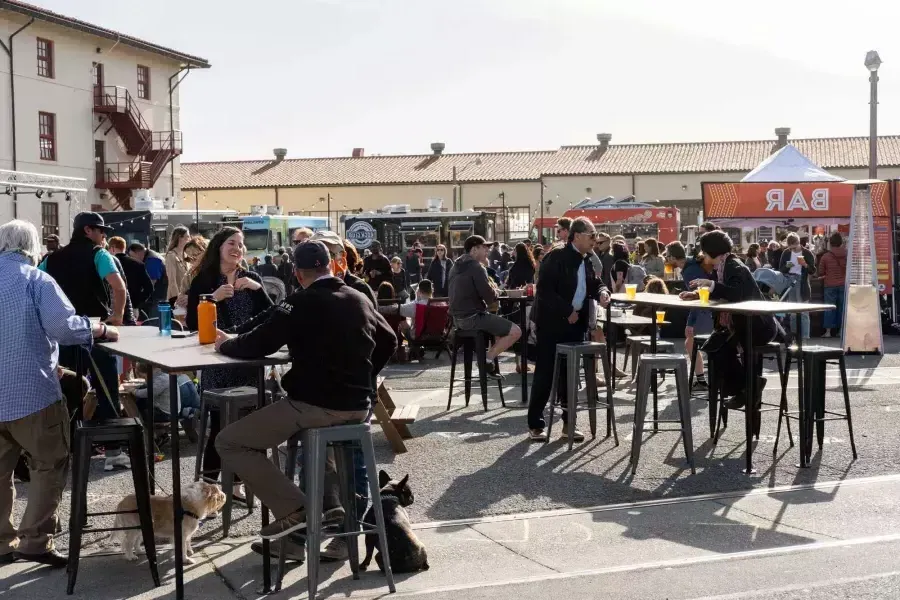 Una folla di persone si riunisce per mangiare ai camion di cibo durante Off the Grid al Fort Mason Center.